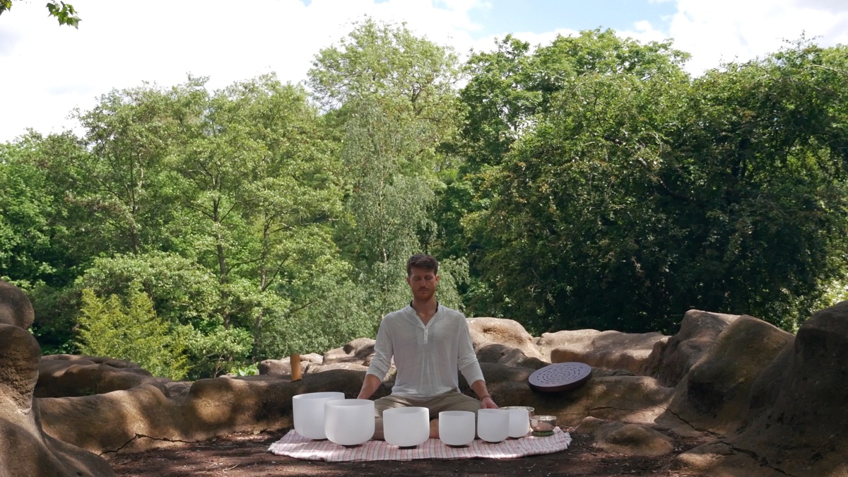 Josh seated in meditation with crystal singing bowls in a woodland clearing